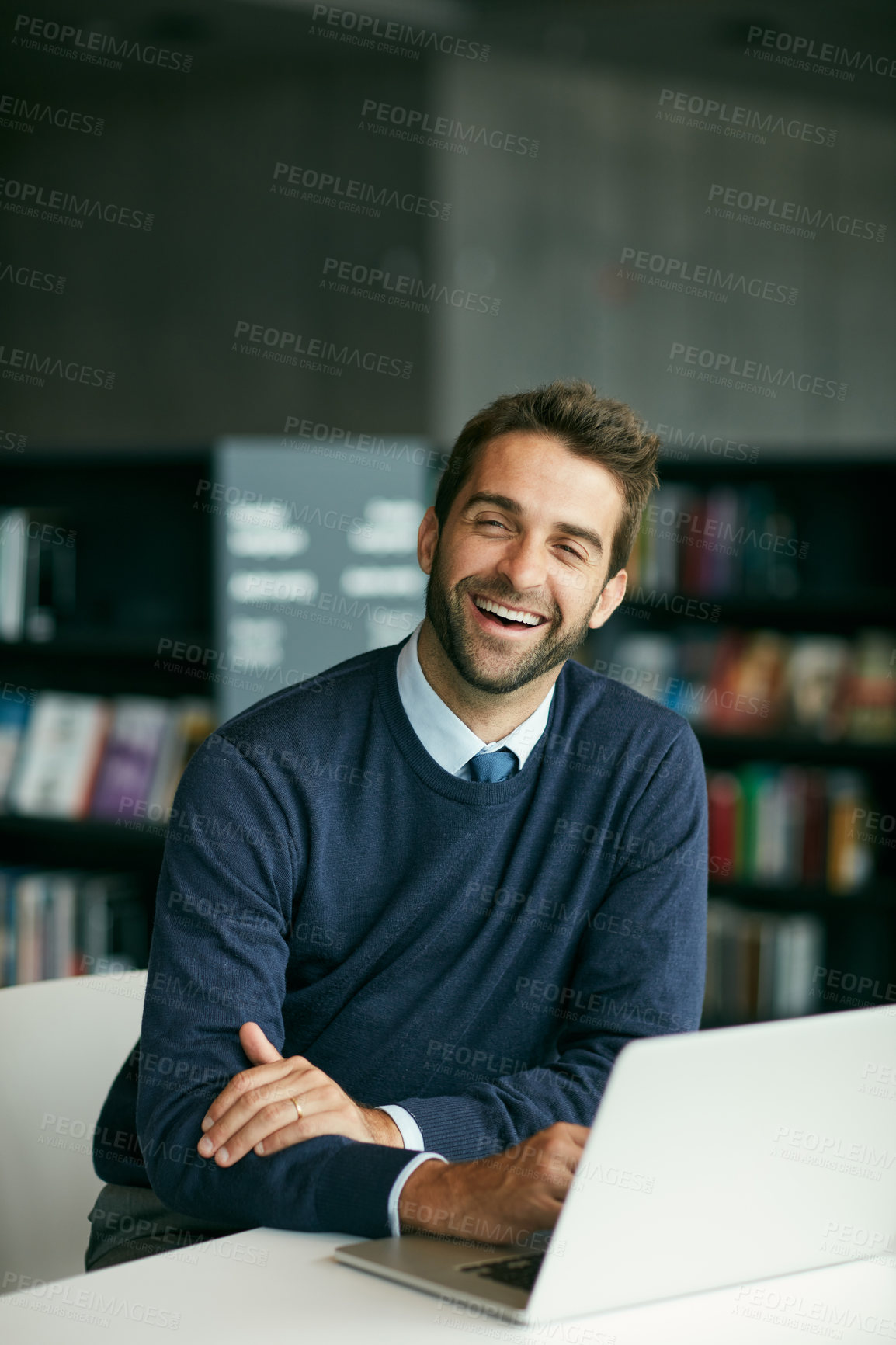 Buy stock photo Cropped shot of a handsome young man sitting in a library alone and laughing while using a laptop