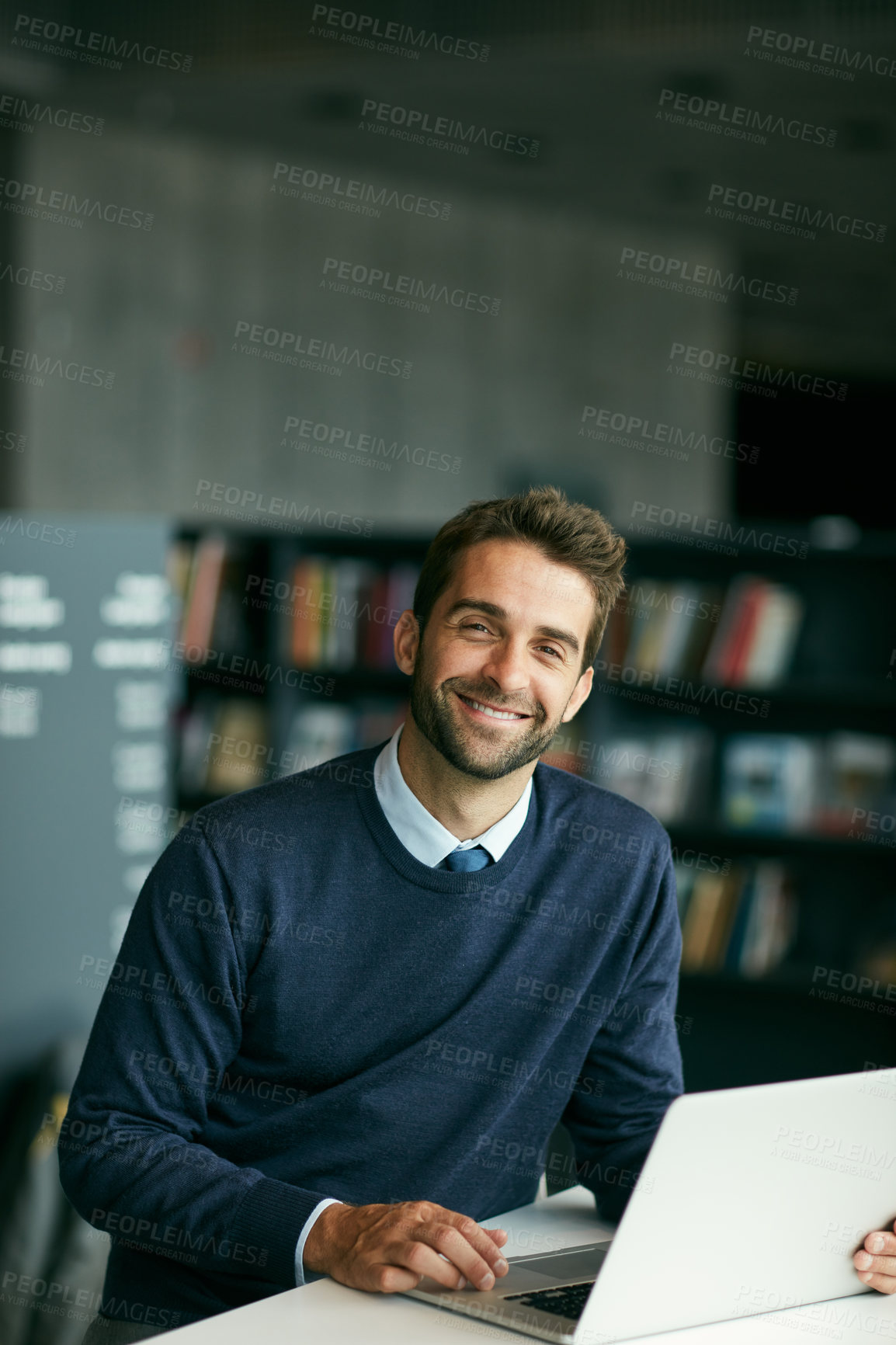 Buy stock photo Cropped portrait of a handsome young businessman sitting alone in a library and using his laptop