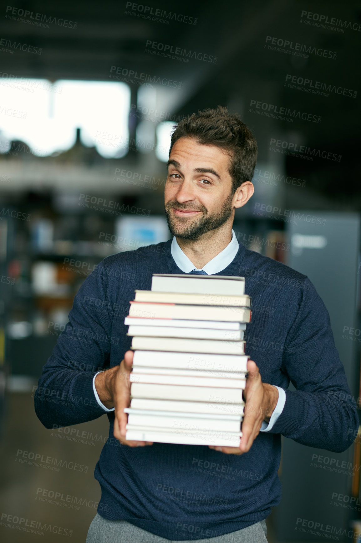 Buy stock photo Cropped portrait of a handsome young businessman standing alone in a library and carrying a pile of books