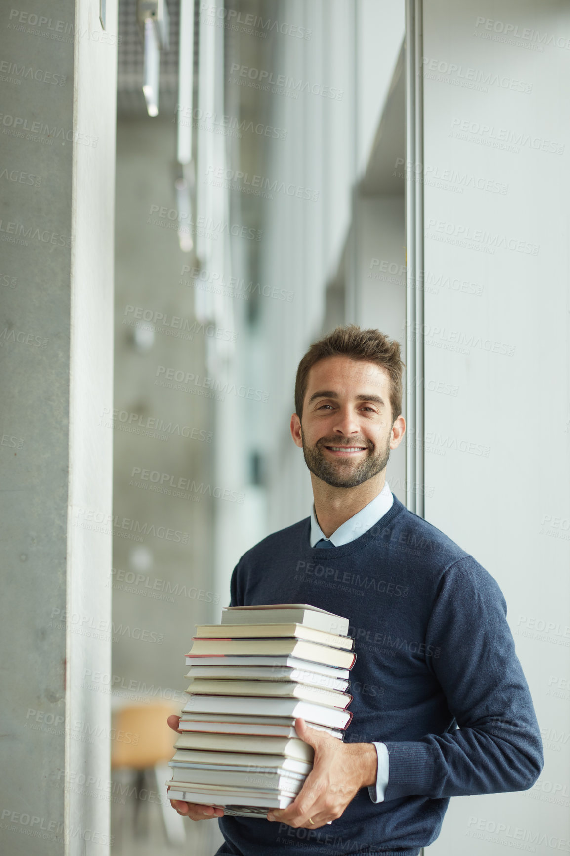 Buy stock photo Cropped portrait of a handsome young businessman standing alone in a library and carrying a pile of books