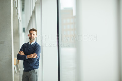 Buy stock photo Cropped portrait of a handsome young businessman standing alone indoors with his arms folded during the day