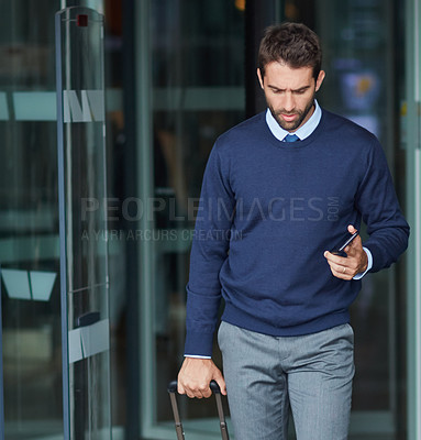 Buy stock photo Cropped shot of a handsome young businessman on the move with a suitcase and his cellphone during the day