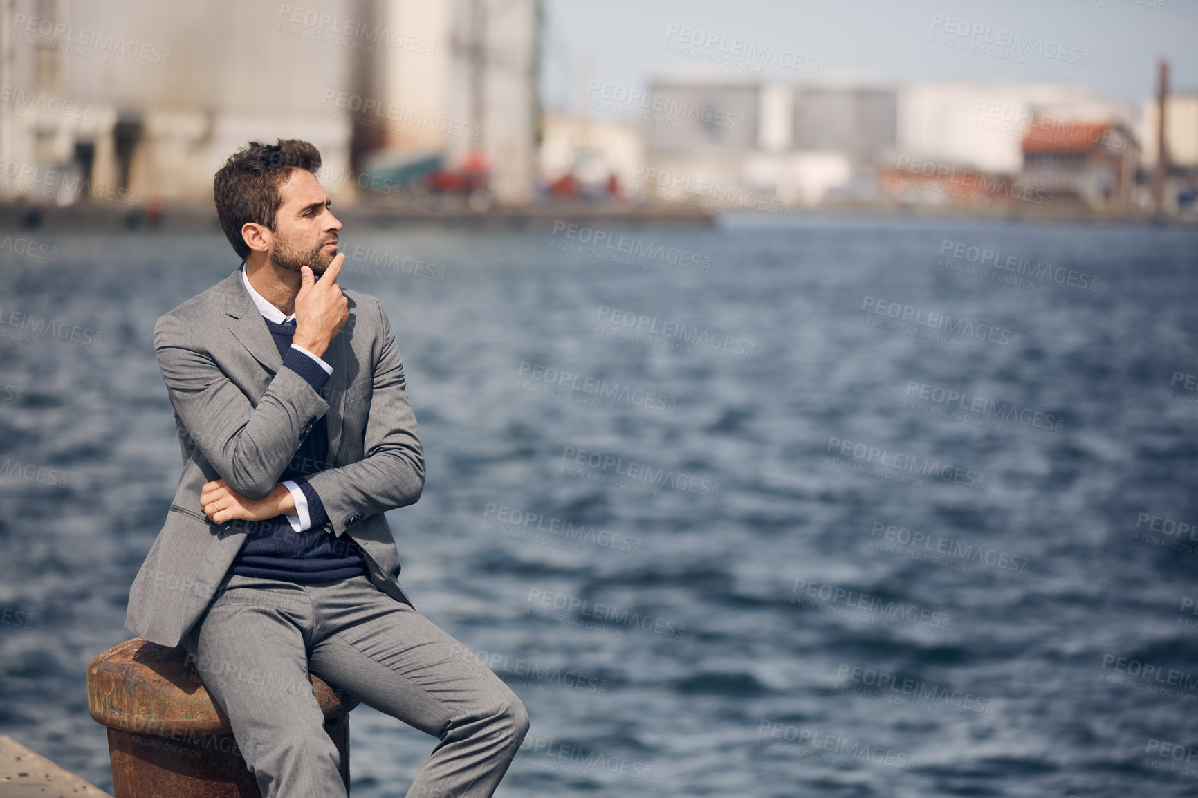 Buy stock photo Cropped shot of a handsome young businessman sitting alone by the harbour and looking contemplative during the day