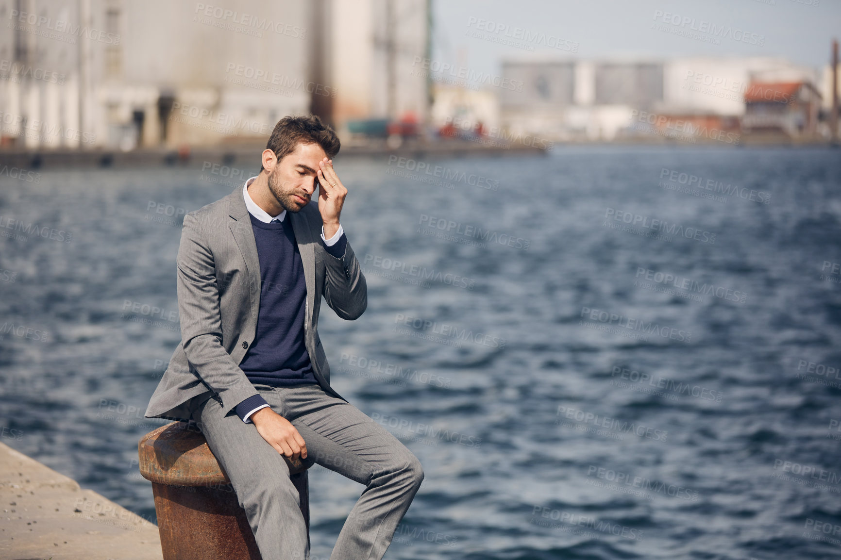 Buy stock photo Cropped shot of a handsome young businessman sitting alone by the harbour and looking stressed during the day