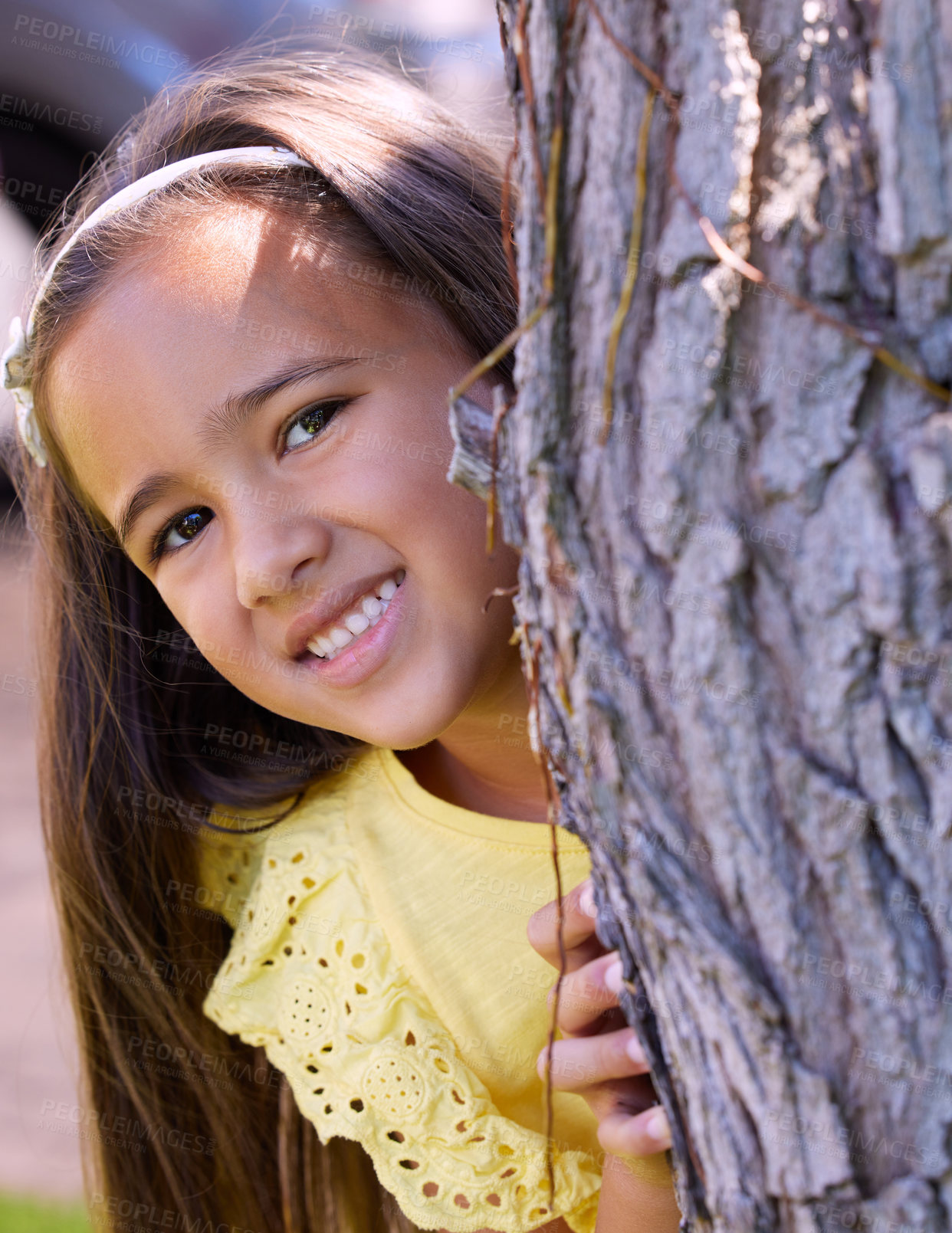 Buy stock photo Shot of an adorable little girl hiding behind a tree