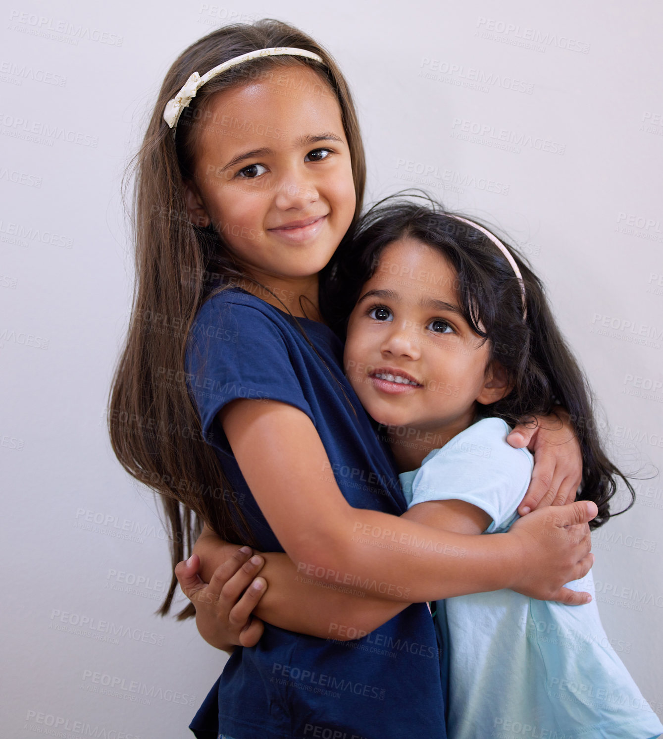 Buy stock photo Children, sisters and hug by wall for portrait with care, bonding and happy with connection in house. Kids, siblings and smile with embrace, love and solidarity with growth at family home in Bogota