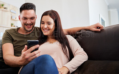 Buy stock photo Shot of a man showing his girlfriend something on his cellphone while sitting at home