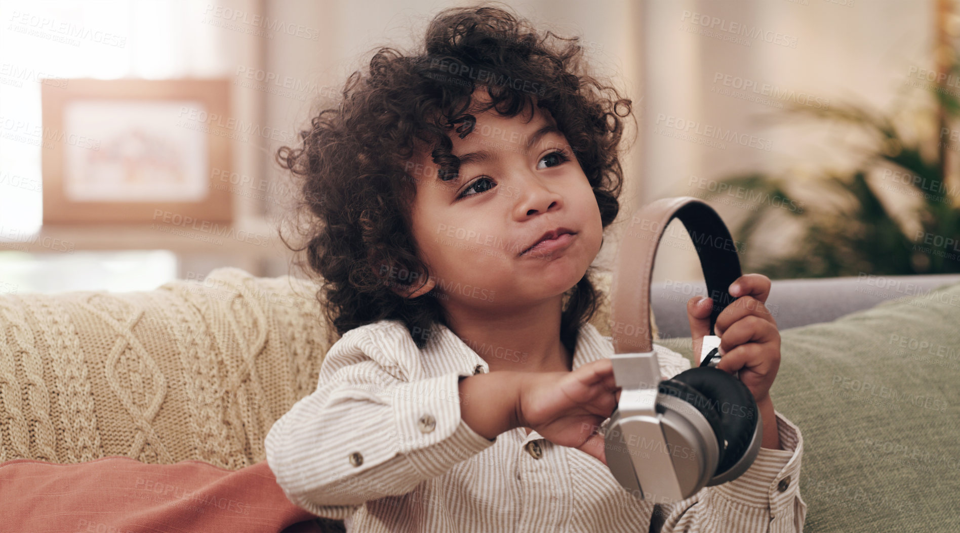 Buy stock photo Shot of an adorable little boy listening to music on headphones while sitting on a sofa at home
