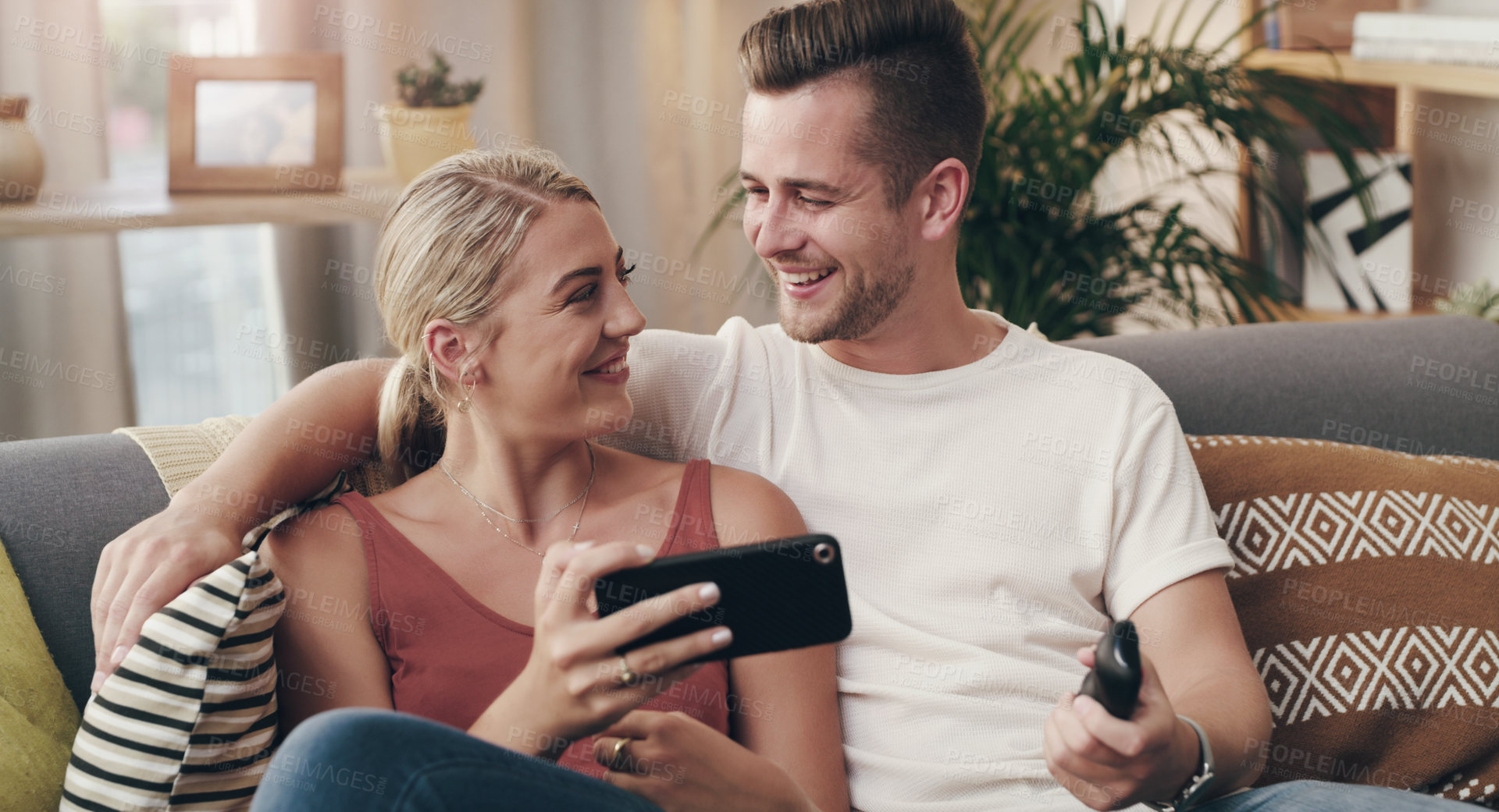 Buy stock photo Shot of a young couple using a smartphone on the sofa