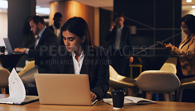 Buy stock photo Shot of a young businesswoman going through paperwork while working on a laptop in an office at night