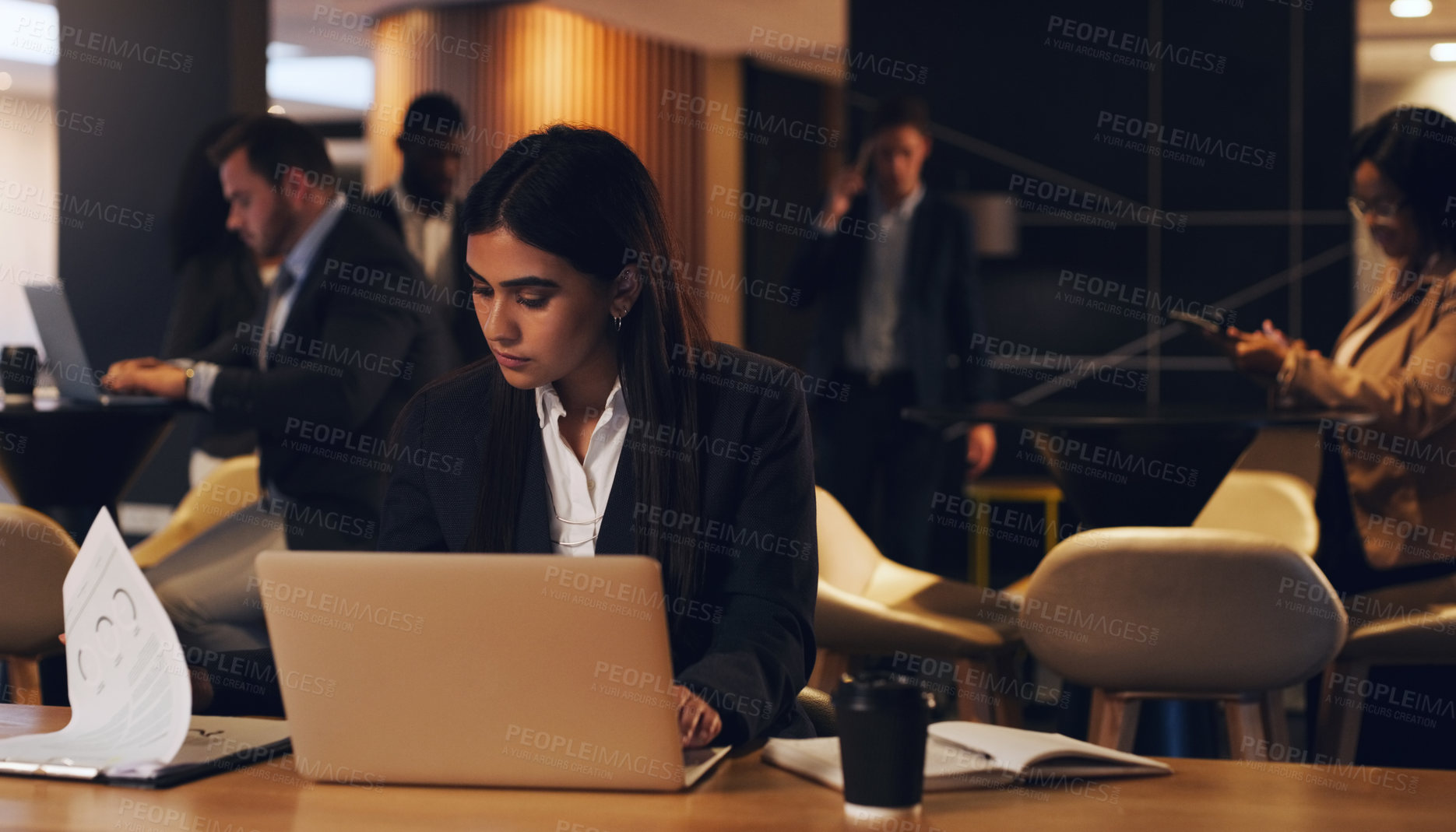 Buy stock photo Shot of a young businesswoman going through paperwork while working on a laptop in an office at night