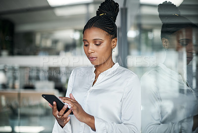 Buy stock photo Shot of an attractive young businesswoman standing alone in the office and using her cellphone during the day