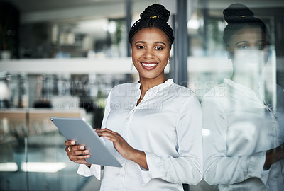 Buy stock photo Shot of an attractive young businesswoman standing alone in the office and using a digital tablet during the day