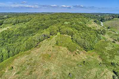 Buy stock photo Aerial view of a field at the top of a hill in the countryside, surrounded by green forestry and trees on a sunny spring or summer day. Scenery of nature with the blue sky on the horizon.