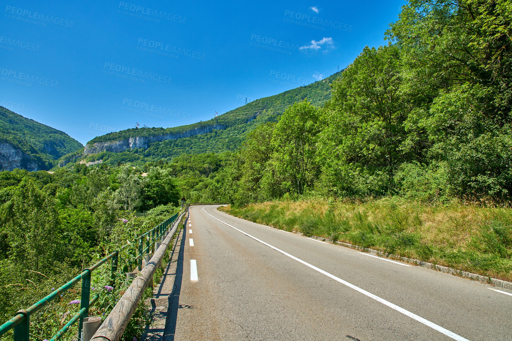 Buy stock photo Countryside road between trees on a blue sky background and copy space. Nature landscape of an empty roadway winding through a forest with wild tree growth in an eco environment on a sunny summer day