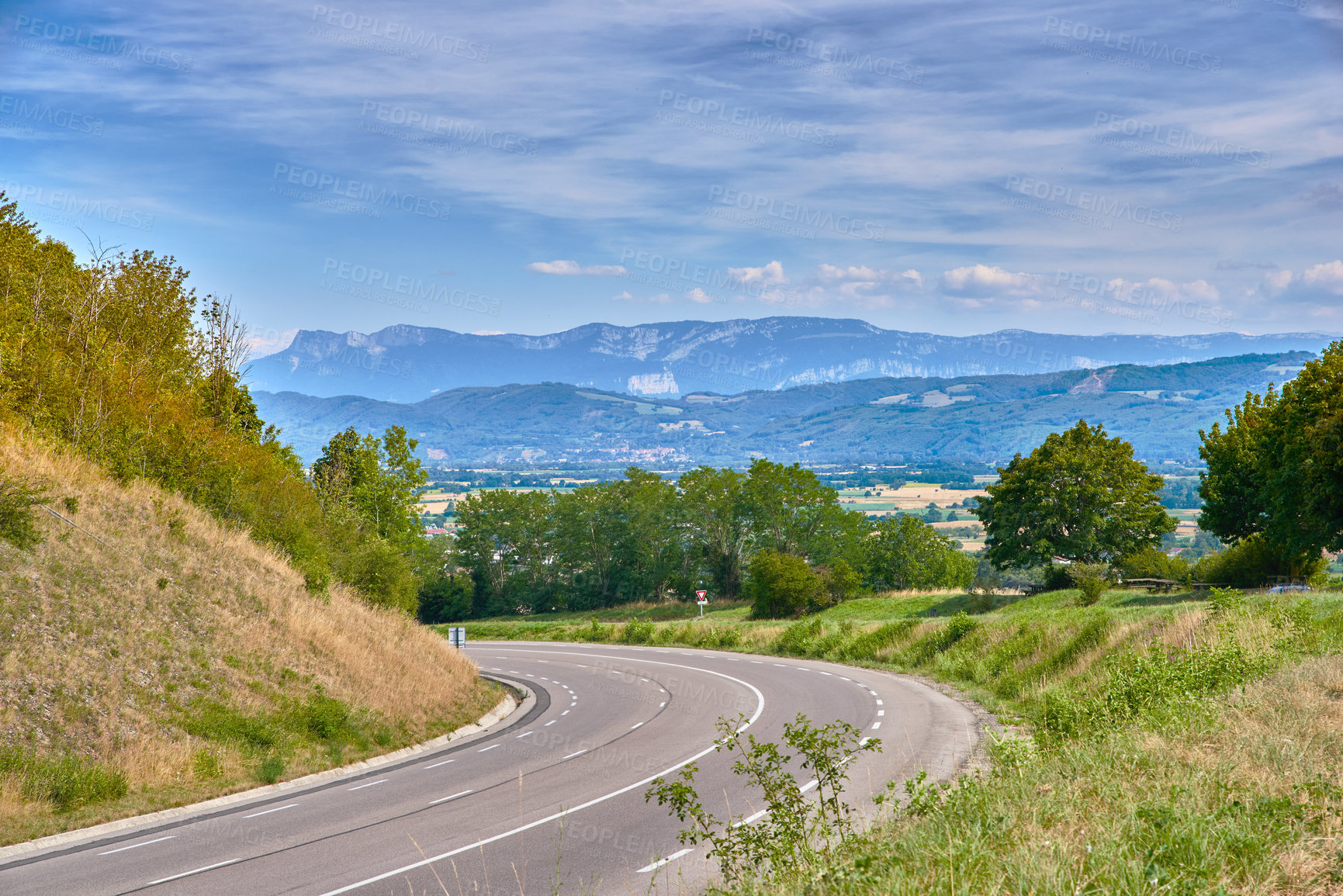 Buy stock photo Scenic countryside route on a sunny day in Summer. Empty curved road with a beautiful view of nature, and a background landscape of the farmlands, mountains and cloudy blue sky.