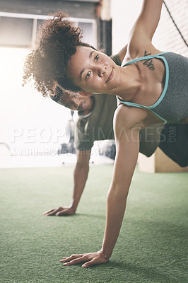Buy stock photo Shot of two sporty young people doing the side plank at the gym