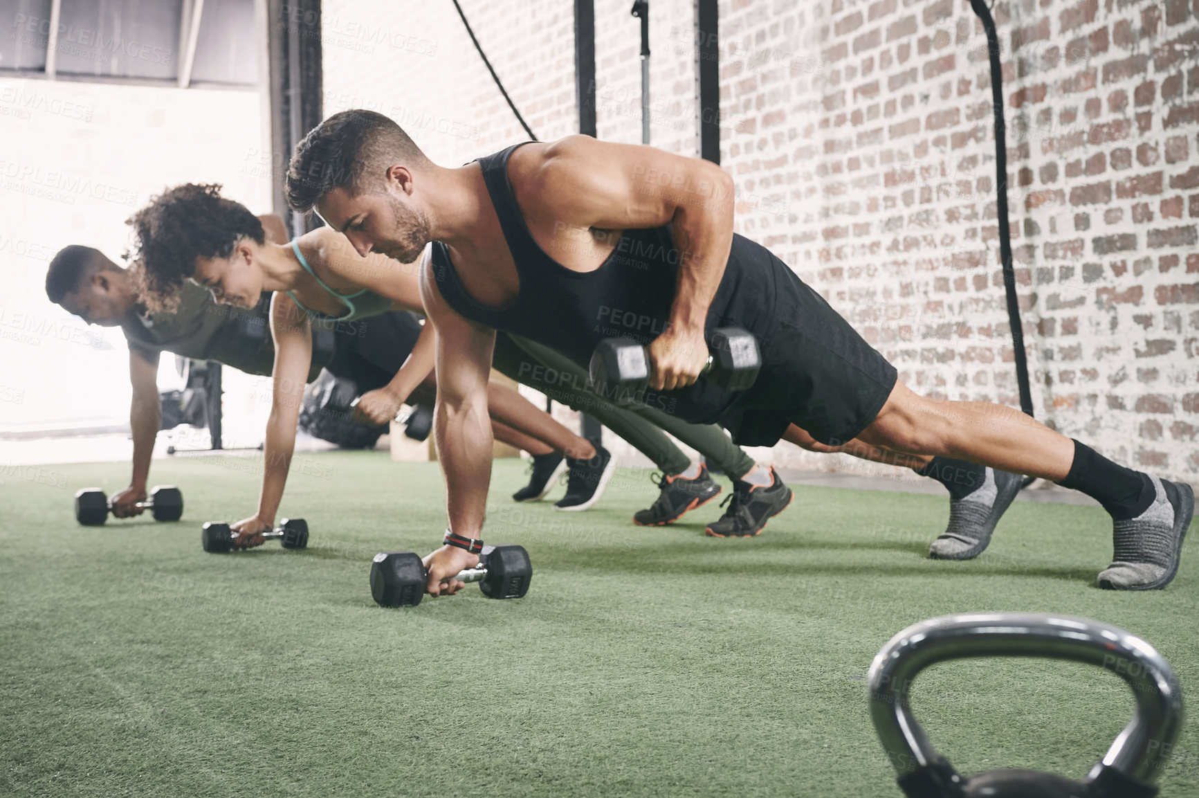Buy stock photo Shot of a fitness group using dumbbells while doing push-ups at the gym