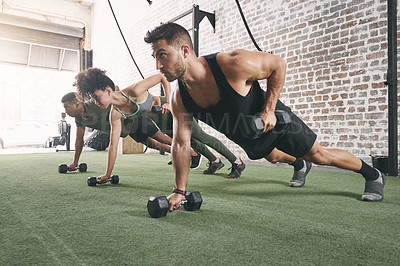 Buy stock photo Shot of a fitness group using dumbbells while doing push-ups at the gym