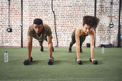 Buy stock photo Shot of two sporty young people using dumbbells while doing push-ups