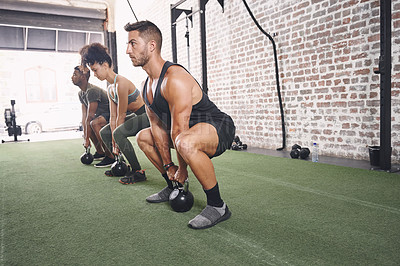 Buy stock photo Shot of a fitness group holding kettlebells while doing squats at the gym