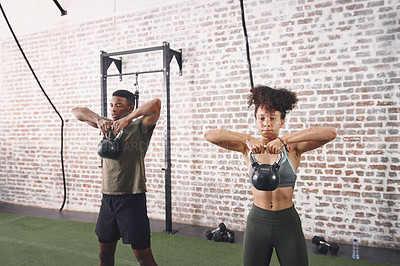 Buy stock photo Shot of two sporty young people using kettlebells while working out at the gym