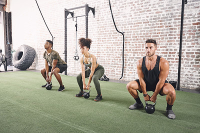 Buy stock photo Shot of a fitness group holding kettlebells while doing squats at the gym