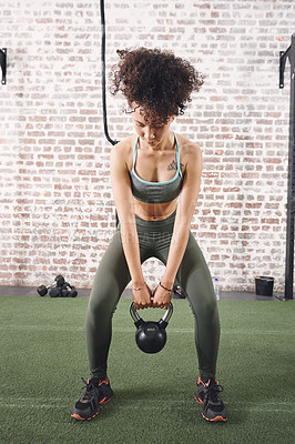 Buy stock photo Shot of a sporty young woman working out with a kettlebell at the gym