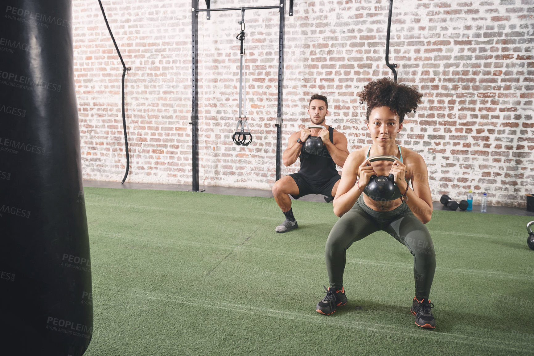 Buy stock photo Shot of two sporty young people using kettlebells while working out at the gym