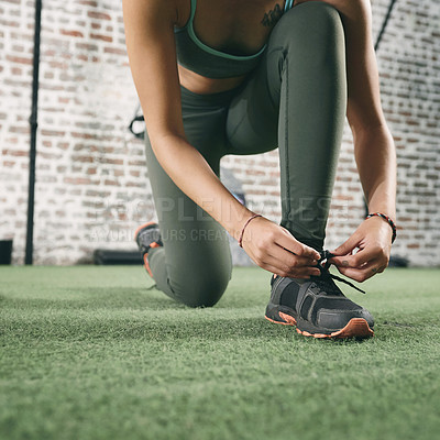 Buy stock photo Cropped shot of a sporty young woman tying her shoelaces at the gym