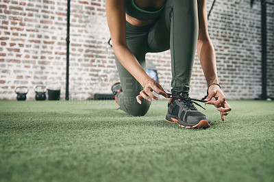 Buy stock photo Cropped shot of a sporty young woman tying her shoelaces at the gym