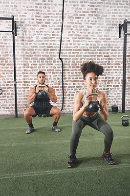 Buy stock photo Shot of two people holding kettlebells while doing squats at the gym