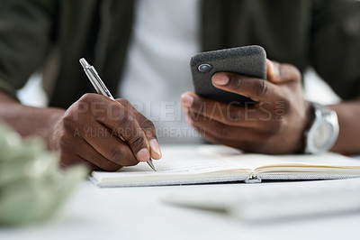 Buy stock photo Cropped shot of a young man using his phone and writing at work