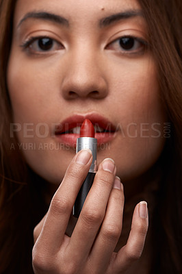 Buy stock photo Cropped portrait of an attractive young woman applying lipstick in studio against a grey background