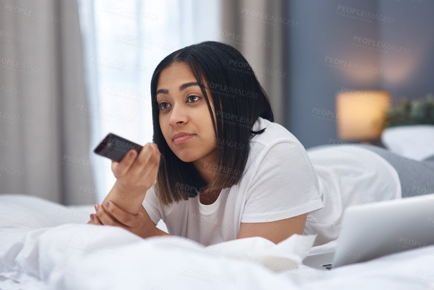 Buy stock photo Shot of a young woman watching television from the comfort of her warm bed