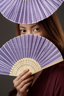 Buy stock photo Cropped portrait of an attractive young woman posing with fans in studio against a grey background