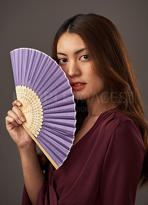 Buy stock photo Cropped portrait of an attractive young woman posing with a fan in studio against a grey background