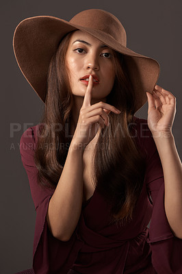 Buy stock photo Cropped portrait of an attractive young woman posing with her finger on her lips in studio against a grey background