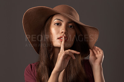 Buy stock photo Cropped portrait of an attractive young woman posing with her finger on her lips in studio against a grey background