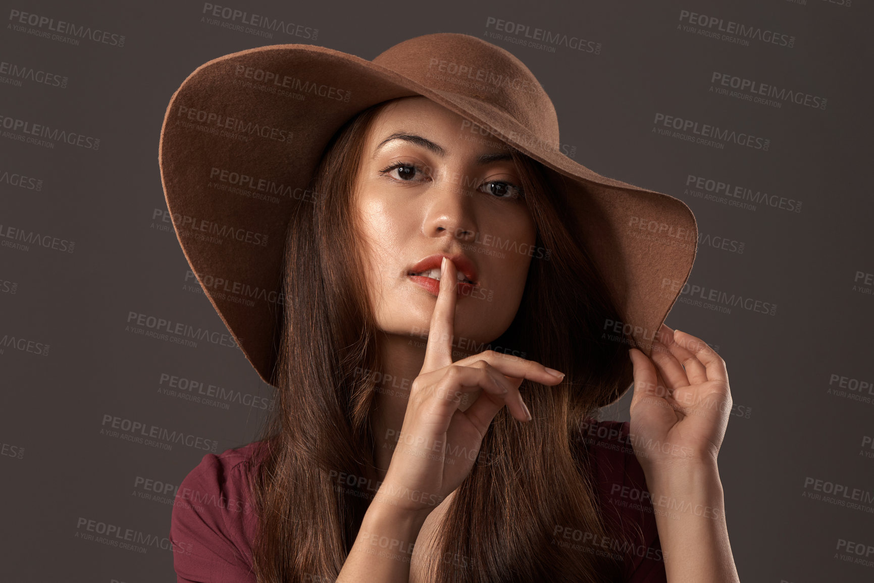 Buy stock photo Cropped portrait of an attractive young woman posing with her finger on her lips in studio against a grey background