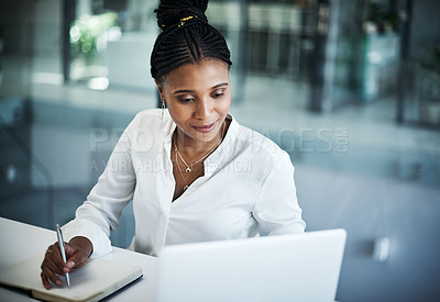 Buy stock photo Shot of an attractive young businesswoman sitting alone in her office and writing notes while using her laptop