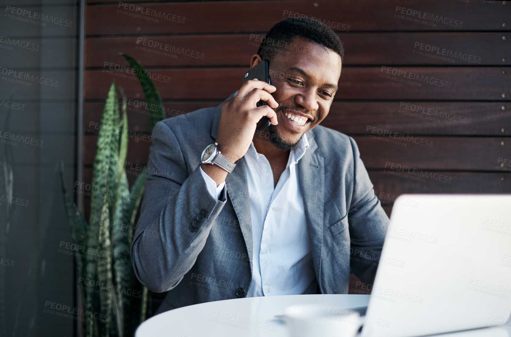 Buy stock photo Shot of a handsome young businessman sitting in the office and using his laptop while talking on his cellphone