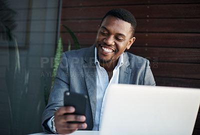 Buy stock photo Shot of a handsome young businessman sitting alone in the office while using his cellphone and laptop
