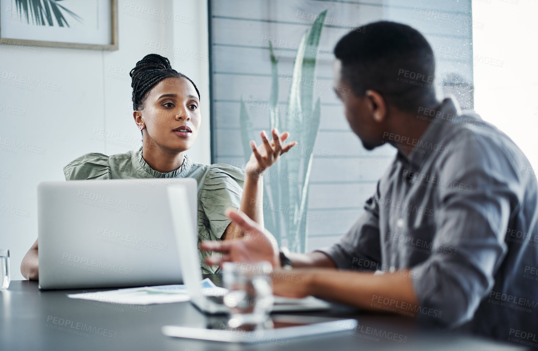 Buy stock photo Shot of two young businesspeople sitting together in the office and having a discussion while using technology