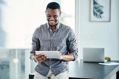 Buy stock photo Shot of a handsome young businessman standing alone in the office and using a digital tablet during the day