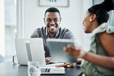 Buy stock photo Shot of two young businesspeople sitting together in the office and having a discussion while using technology