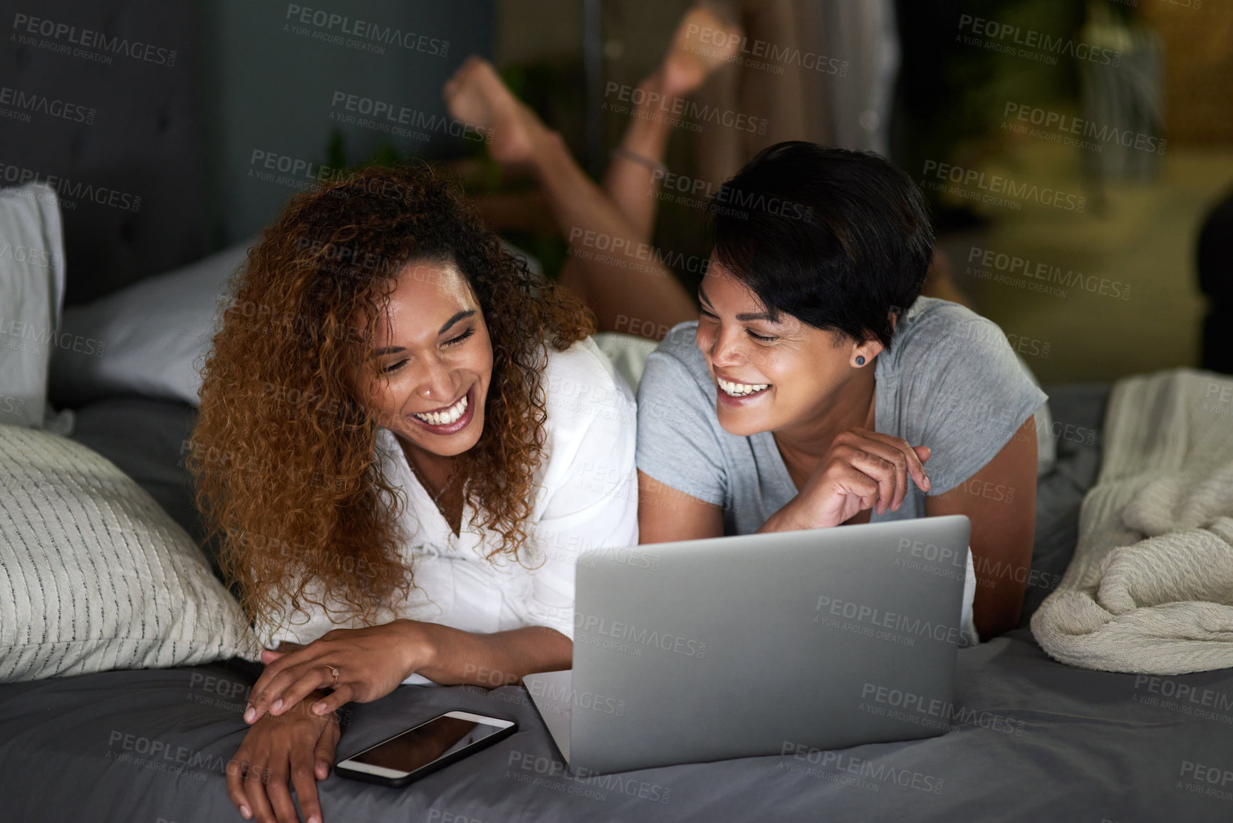 Buy stock photo Shot of a young couple using a laptop while lying on their bed