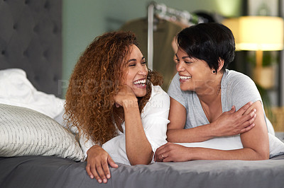 Buy stock photo Shot of a young couple laughing while lying on their bed together