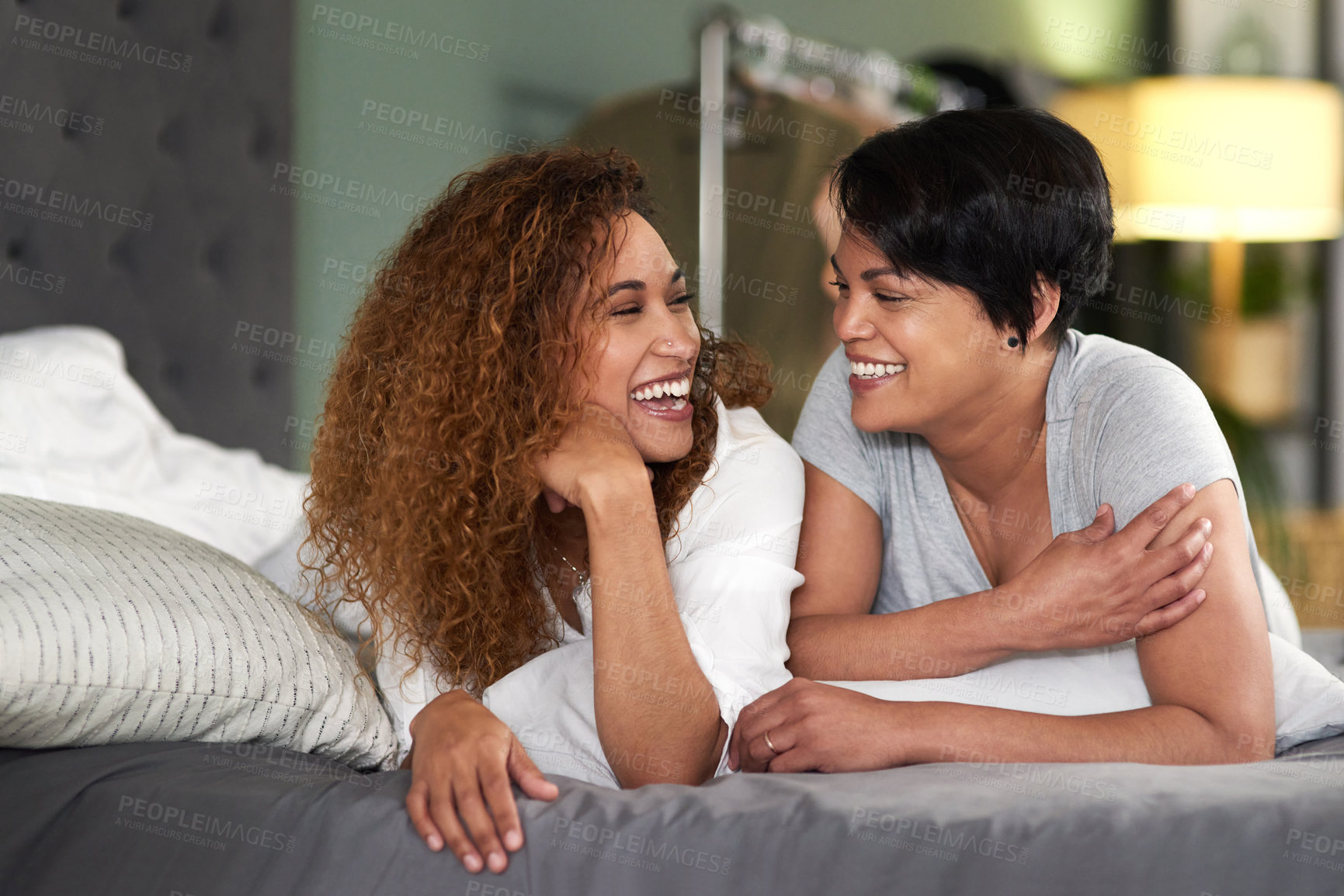 Buy stock photo Shot of a young couple laughing while lying on their bed together