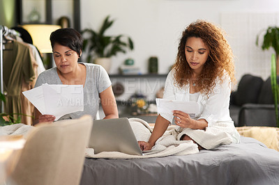 Buy stock photo Shot of a young couple holding paperwork and using a laptop while sitting at home